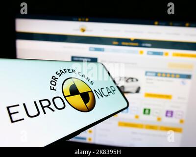 Telefono cellulare con logo del programma di sicurezza auto Euro NCAP sullo schermo di fronte al sito web. Messa a fuoco al centro del display del telefono.