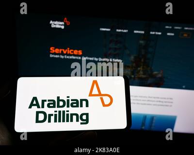 Persona che tiene il cellulare con il logo dell'azienda Saudita Arabian Drilling Company (ADC) sullo schermo di fronte alla pagina web. Messa a fuoco sul display del telefono. Foto Stock