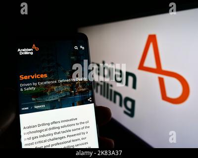 Persona che tiene il cellulare con la pagina web dell'azienda Saudita Arabian Drilling Company (ADC) sullo schermo con il logo. Messa a fuoco al centro del display del telefono. Foto Stock