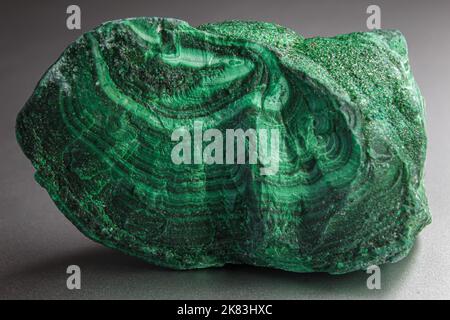 Pietra a pelo di malachite in cima alla superficie argentata. Pietra verde a forma casuale con onde e sfumature di colore verde. La malachite è un rame verde Foto Stock