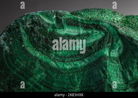 Pietra a pelo di malachite in cima alla superficie argentata. Pietra verde a forma casuale con onde e sfumature di colore verde. La malachite è un rame verde Foto Stock