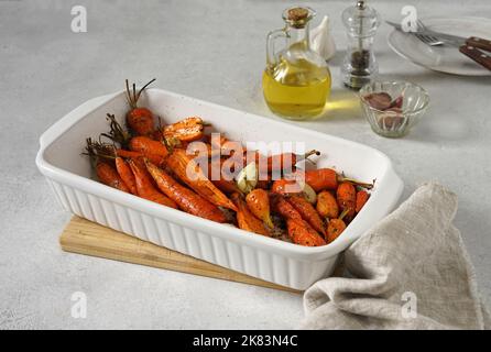 Carote fritte con erbe nella teglia da forno su un tavolo leggero, cibo vegano Foto Stock