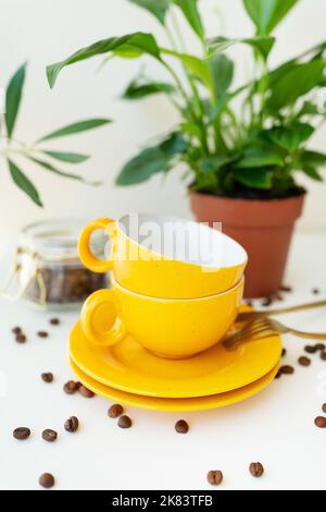 Bella mattina, il processo di preparazione del caffè. La macchina per caffè all'americana è dotata di una tazza gialla su un tavolo bianco e di chicchi di caffè sparsi Foto Stock