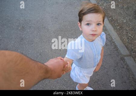 il ragazzo di 3 anni tiene la mano del padre per attraversare la strada. Punto di vista Foto Stock