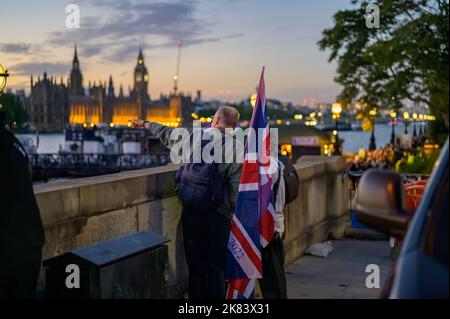 Londra - 17 settembre 2022: L'uomo detiene la bandiera di Union Jack e punta verso le Camere del Parlamento. Luce di prima serata Foto Stock