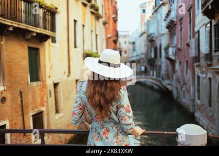 Vista da dietro l'elegante solista donna turistica in abito floreale con cappello visita a Venezia, Italia. Foto Stock