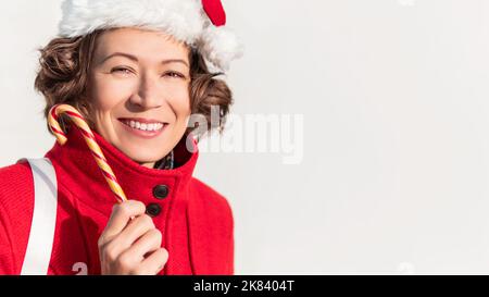 Donna riccia con canna da zucchero a righe. Bella femmina con frusta di liquirizia di Natale. Banner con spazio di copia. Foto Stock
