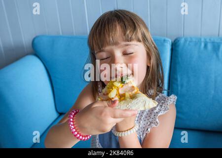 La bambina carina mangia la pizza. I bambini pranzano in una caffetteria, primo piano Foto Stock