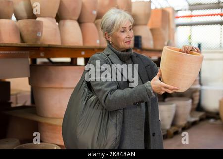 Donna anziana che sceglie le pentole per le piante della casa nel mercato di giardinaggio Foto Stock