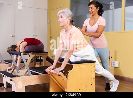 La donna ispanica pilota l'istruttore aiutando la donna anziana esercitandosi sulla sedia della wunda Foto Stock