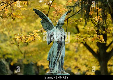 bel angelo vecchio con le ali di fronte alle foglie d'autunno dorato in un cimitero Foto Stock