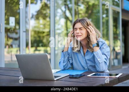 Una giovane imprenditrice delusa si sentiva frustrato, seduto con un notebook all'aperto per strada, guardando in alto e lamentandosi Foto Stock