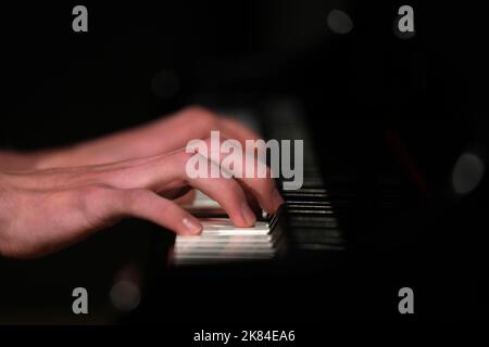 Un primo piano di un pianista mani e dita che suonano i tasti su un pianoforte. Isolato su uno sfondo annerito con alcune luci sfocate e riflessi Foto Stock