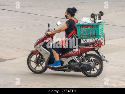 SAMUT PRAKAN, THAILANDIA, ottobre 03 2022, Una donna in grembiule trasporta un carico su una motocicletta Foto Stock