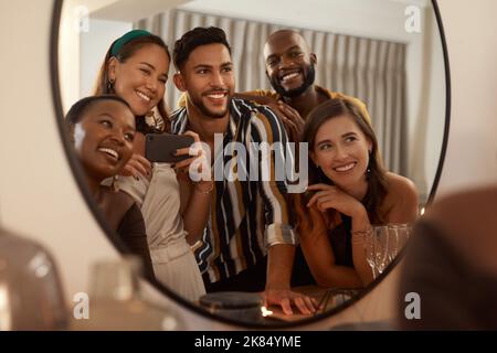 Possiamo continuare a creare ricordi epici insieme: Un giovane gruppo di amici che usa un cellulare per scattare selfie speculari durante una cena di Capodanno. Foto Stock