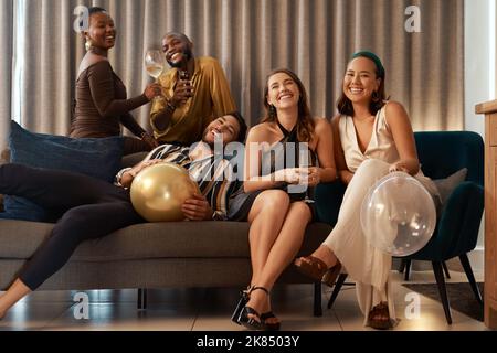 In attesa che la palla scenda. Un gruppo di amici diversi seduti nel soggiorno insieme durante una festa di Capodanno a casa. Foto Stock