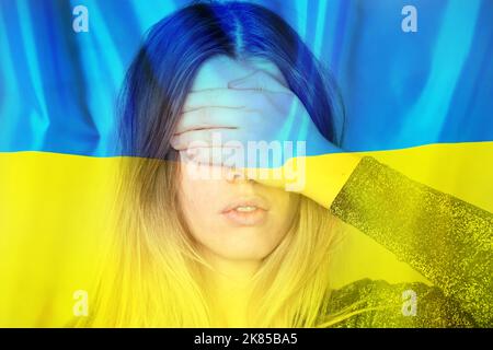 La ragazza chiuse gli occhi con la mano sullo sfondo della bandiera nazionale e stemma dell'Ucraina, giallo-blu, pace in Ucraina, nessuna guerra, Foto Stock