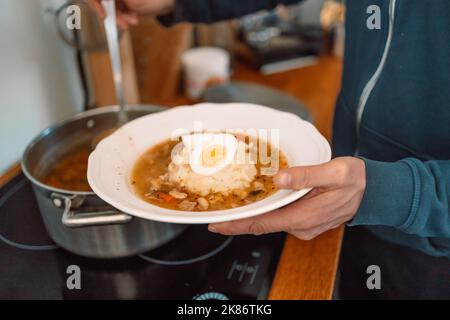 Zuppa acida tradizionale polacca Zurek in ciotola di ceramica. L'uomo versa la zuppa in una ciotola Foto Stock