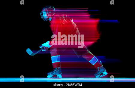 Lancio potente. Giocatore di hockey su ghiaccio maschile in uniforme protettiva sportiva in azione su sfondo scuro in luce mista al neon. Raggiungimento, obiettivi Foto Stock