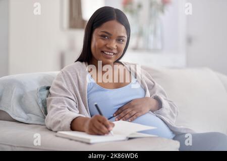 Io scherzo giù ogni calcio e ogni altra sensazione. Una donna incinta che scrive nel suo notebook mentre seduto sul divano a casa. Foto Stock