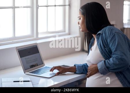 Il medico ha detto di prendere facile, non fare nulla. Una donna incinta che usa il suo computer portatile mentre si siede a casa. Foto Stock