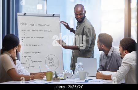 Mettendo insieme tutte le loro idee, un giovane uomo d'affari che presenta un incontro ai suoi colleghi in una sala riunioni. Foto Stock