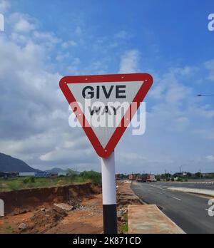 Un cartello di give way sulla strada sotto il cielo blu Foto Stock