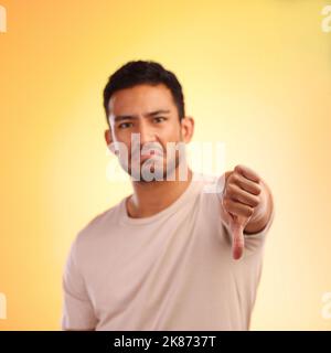 Un giovane che mostrava pollici giù mentre si trovava su uno sfondo giallo. Foto Stock