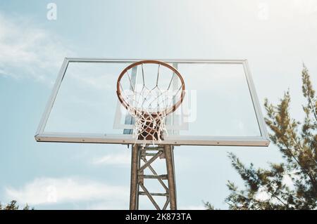 Pallacanestro, sport e fitness con un cerchio su un campo per una partita, una partita o un evento competitivo all'aperto dal basso. Esercizio, allenamento e rete con lo sport Foto Stock