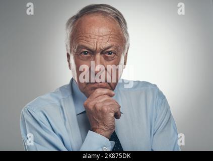 Ho un ultimo piano come CEO: Un uomo d'affari anziano che si trova da solo su uno sfondo grigio in studio e che guarda contemplativo. Foto Stock