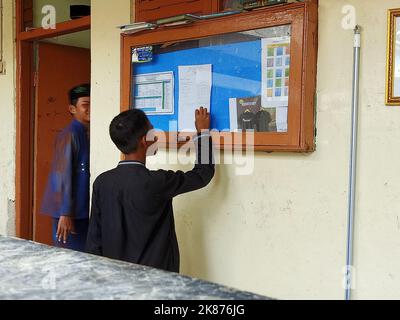 Un ragazzo sta osservando il contenuto della bacheca di fronte alla classe di un collegio islamico tradizionale Foto Stock