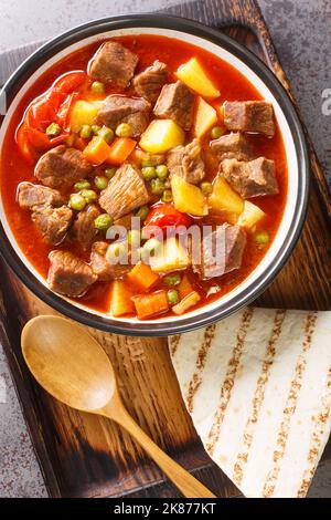 Orman Kebab? è un succoso piatto di carne che ha molti piselli e patate affettate closeup nel recipiente sul tavolo. Vista verticale dall'alto Foto Stock