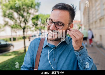 Calma il giovane adulto bell'uomo, mettendo gli auricolari in entrambe le orecchie, assicurandosi che si adattino, ascoltando la musica. Foto Stock