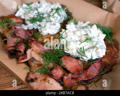 Croccante arrosto di patate con pancetta fritta e condita con una salsa di yogurt riccante. Frittelle di patate servite con pancetta croccante e panna acida, selezione di fo Foto Stock