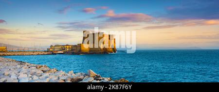 Napoli, Italia. Castel dell'Ovo con rocce frangiflutti in primo piano e con un bel cielo tramonto. Intestazione banner. Foto Stock