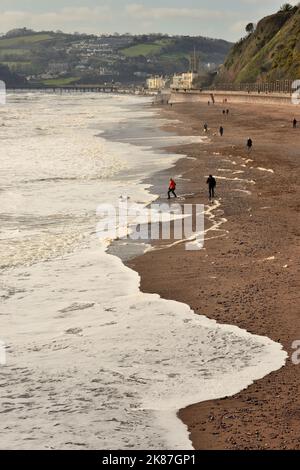 Persone che camminano sulla spiaggia come schiuma si raccoglie su una marea in arrivo. Foto Stock