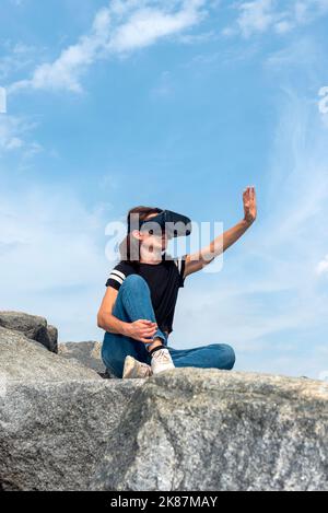 Donna che indossa un visore VR che raggiunge il cielo. Foto Stock
