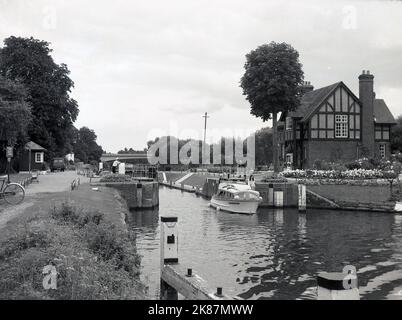 1966, storico, una barca che attraversa Bray lock sul fiume Tamigi a Windsor & Eton lungofiume, Inghilterra, Regno Unito, con il cottage custodi serratura su l'isola tra la serratura e lo stramazzo, visto sulla destra della foto. Il blocco sul lato erba è stato costruito nel 1845. Foto Stock