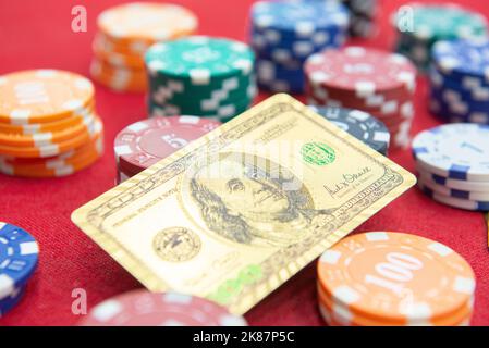 Vista dall'alto delle carte da gioco dorate da 100 dollari accanto alle pile di fiches sul tavolo in feltro rosso. Il gioco di poker è uno dei giochi di carte più popolari al mondo A. Foto Stock