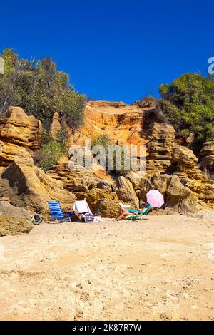 Donna che guarda il telefono, prendere il sole su una sedia a sdraio Playa Sancti Petri spiaggia, Costa de la Luz, Cadice, Spagna Foto Stock