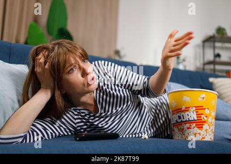 Donna frustrato che guarda la TV mentre si siede sul divano di casa Foto Stock