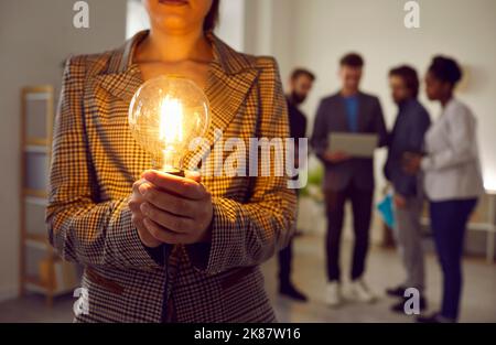 Primo piano della lampada Edison incandescente nelle mani di una donna che la tiene in ufficio. Foto Stock