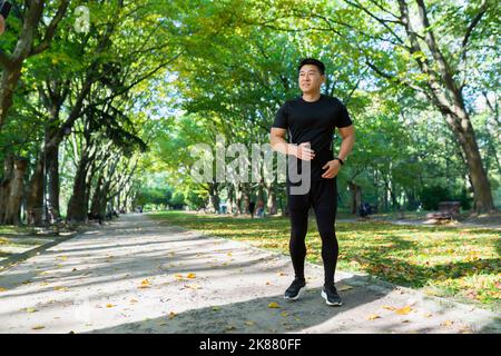 Ritratto completo, uomo asiatico in corsa in ufficio parco, uomo in abbigliamento sportivo nelle giornate di sole, sorridente e felice di fitness. Foto Stock