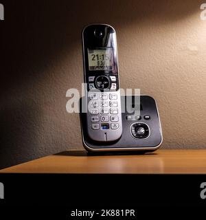 Un telefono wireless nero con supporto sul tavolo nella stanza buia Foto Stock