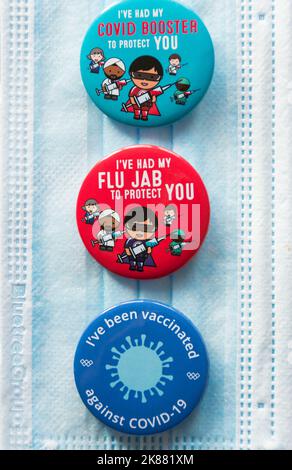 Colorati badge Covid 19 Booster e Flu Jab che si appoggiano su un cordino NHS Foto Stock