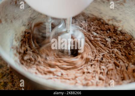 Primo piano di pastella per torte al cioccolato e fiore nel recipiente di miscelazione con fruste rotanti. Foto Stock