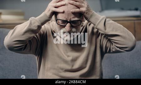 Uomo anziano con demenza che ha mal di testa e che tocca la testa Foto Stock