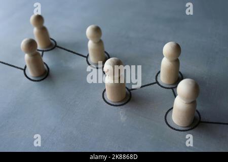 Catena di immagini a fuoco selettivo di bambole in legno collegate da linee. Concetto di cooperazione, interazione, comunicazione e diffusione dell'informazione Foto Stock