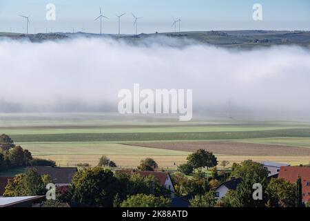 Un gruppo di mulini a vento si erge su una collina contro un cielo limpido e c'è nebbia nella valle di fronte ad essa. Foto Stock