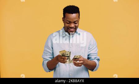 felice uomo afroamericano che conta le banconote del dollaro isolate sul giallo Foto Stock